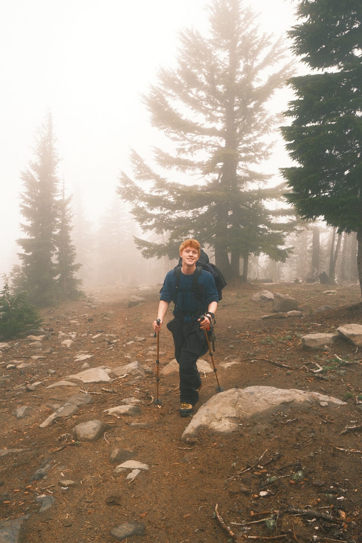 Josiah on a foggy trail between tall conifers.
